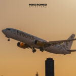 Boeing 737 de Flybondi matrícula LV-KDQ despegando con el tren de aterrizaje aún desplegado, con luz de atardecer y la silueta de un edificio alto de fondo