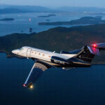 Jet ejecutivo Embraer Phenom 300 matrícula N373EE en vuelo al atardecer, con librea blanca y negra, sobre un paisaje de islas y agua