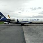 Bombardier CRJ200 LV-JOI de Joy Airline con librea azul y blanca estacionado en plataforma, con titulado JOY en el fuselaje y un tractor de remolque en el tren de nariz