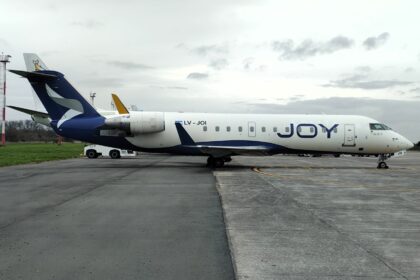 Bombardier CRJ200 LV-JOI de Joy Airline con librea azul y blanca estacionado en plataforma, con titulado JOY en el fuselaje y un tractor de remolque en el tren de nariz
