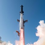 Cohete Starship de SpaceX despegando desde la torre de lanzamiento, con llamas y vapor en la base y cielo azul con nubes