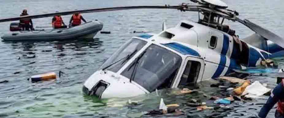 Helicóptero blanco con franjas azules parcialmente sumergido en el lago de Atitlán, Guatemala, con restos flotando alrededor y rescatistas con chalecos naranja en una embarcación inflable al fondo
